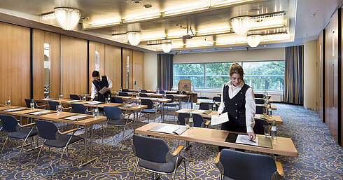 Le personnel prépare une salle de réunion au Maritim Hotel Frankfurt avec sièges en rangée et vue sur la verdure.