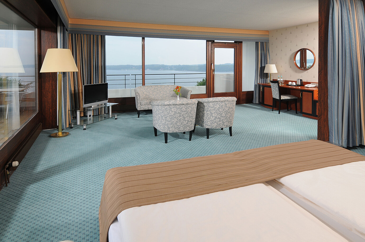 Junior Suite del Maritim Hotel Kiel, con area salotto, scrivania, TV e ampia finestra frontale con vista sul mare.