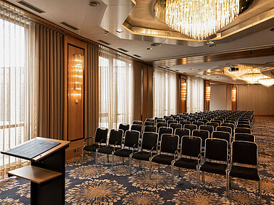 Gran sala de conferencias con sillas en fila, atril y lámparas en el Maritim Hotel Ulm.