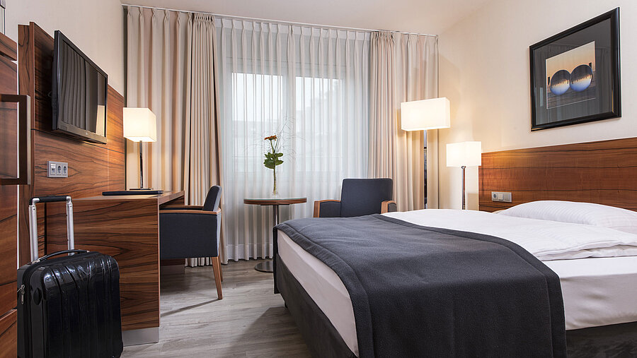 Camera accogliente con letto doppio, scrivania e valigia al Maritim Hotel Monaco