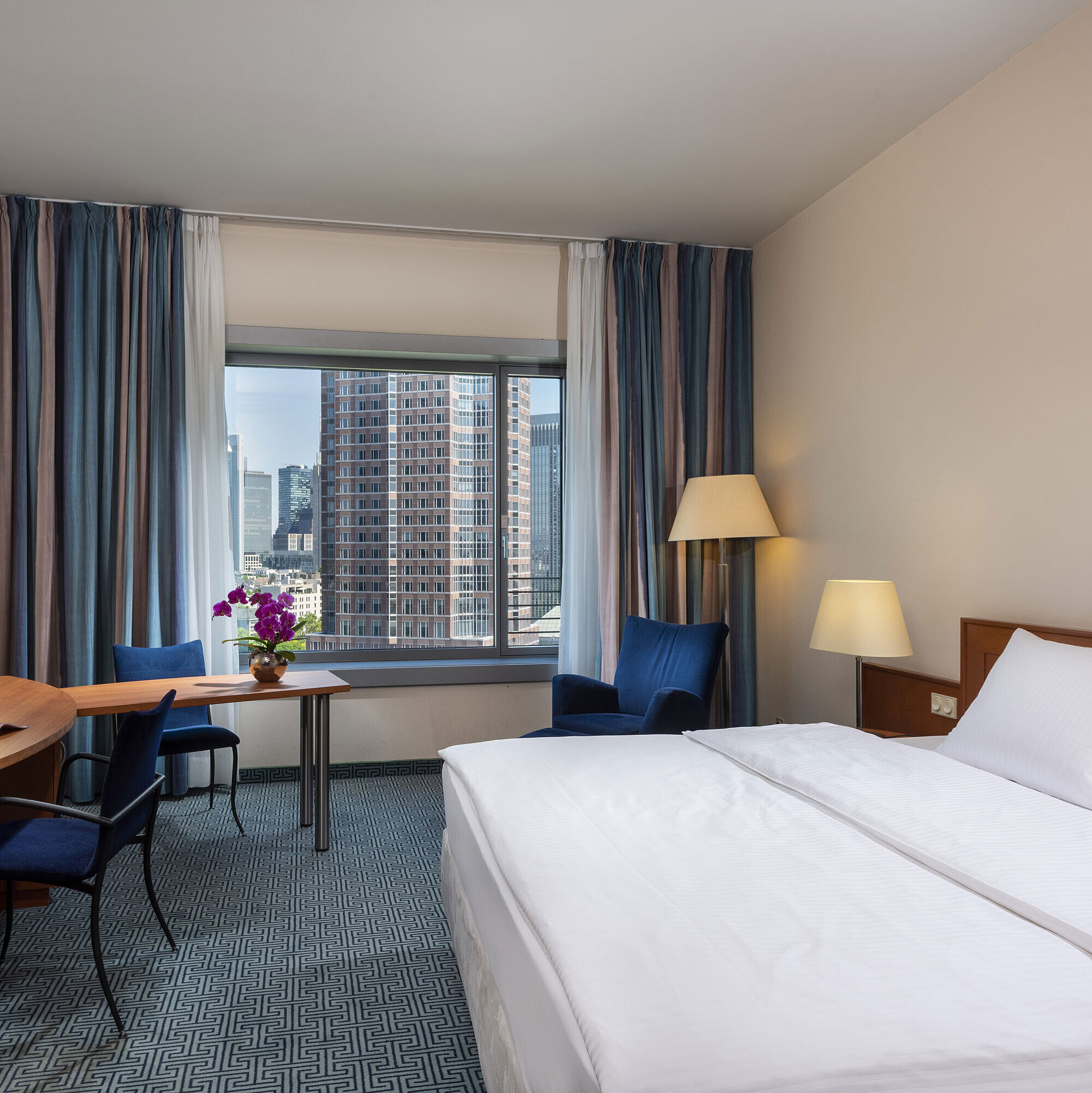 Camera Superior del Maritim Hotel Frankfurt con letto matrimoniale, scrivania e vista sullo skyline di Francoforte.