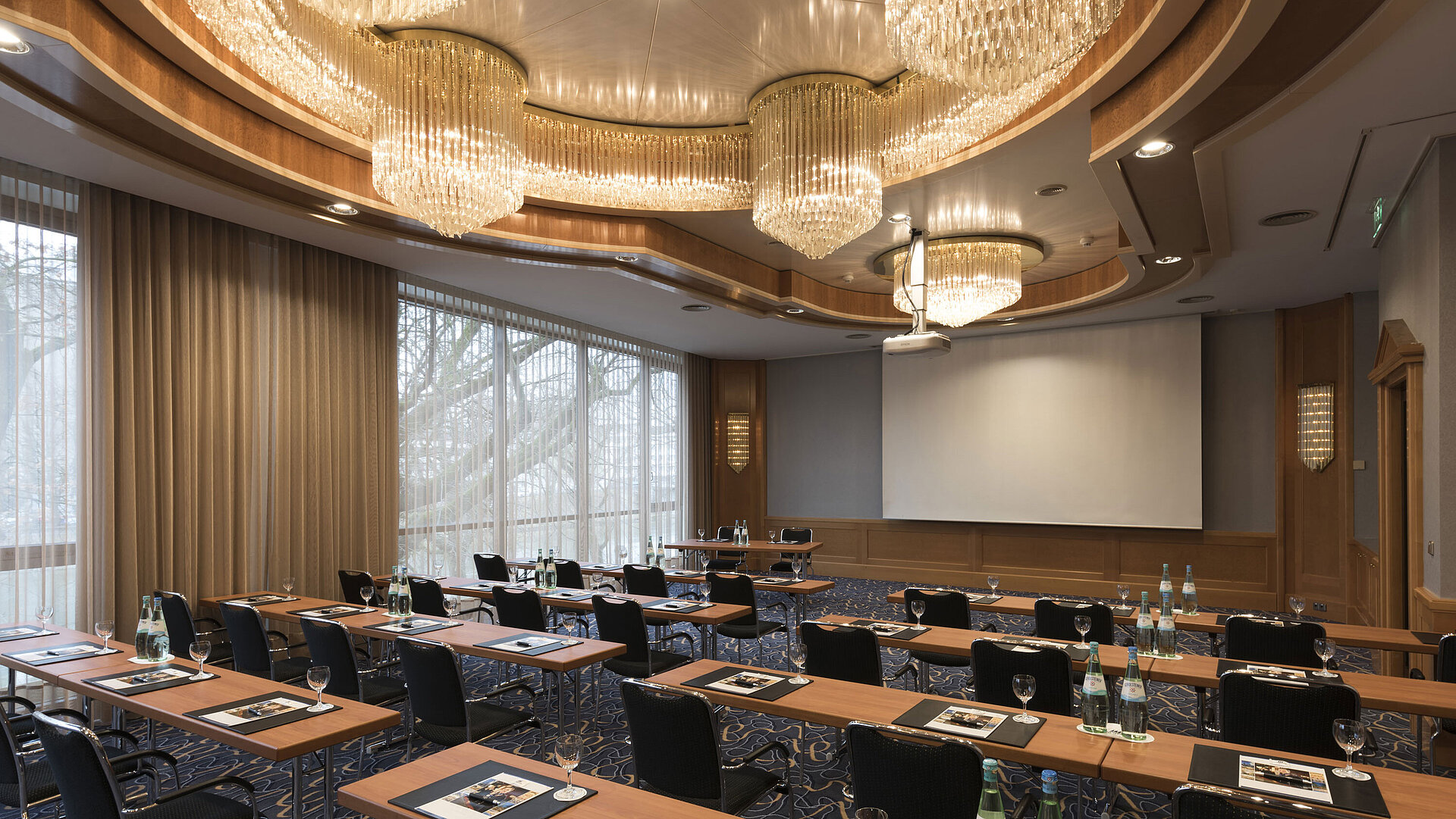 Sala de conferencias elegante con sillas en fila, lámparas y pantalla en el Maritim Hotel Ulm.