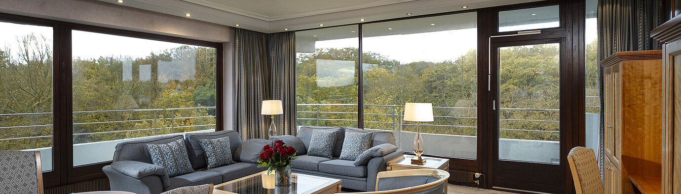 Soggiorno della Grand Suite al Maritim Hotel Kiel con ampie finestre, arredi eleganti e vista sul verde.
